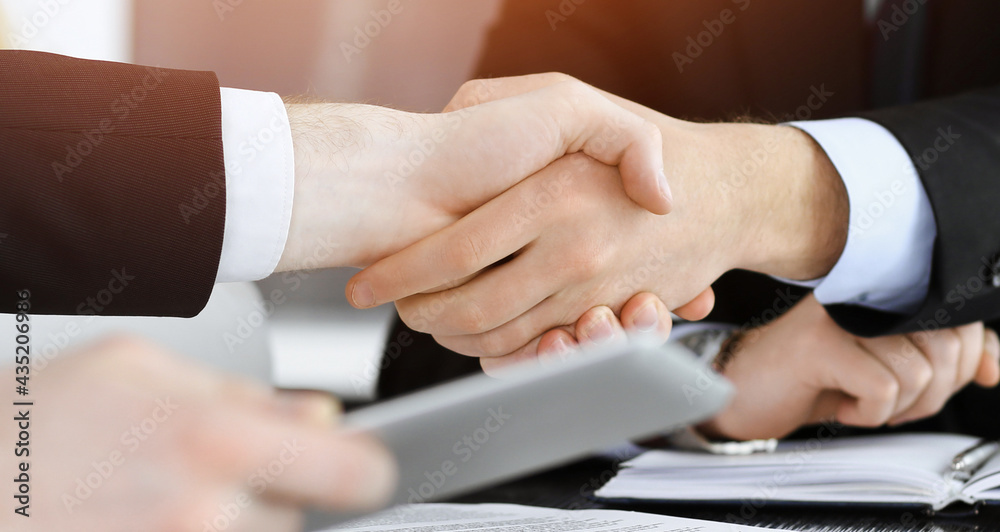 Obraz premium Businessman shaking hands with his colleague above the glass desk in sunny modern office, close-up. Unknown business people at meeting