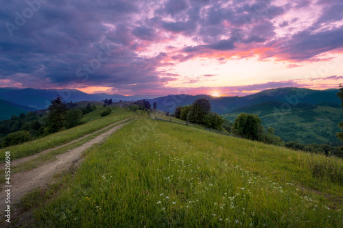Dramatic colorful summer sunset sky over mountain hill with the rural road. Carpathian mountains. Ukraine.