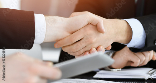 Businessman shaking hands with his colleague above the glass desk in sunny modern office, close-up. Unknown business people at meeting