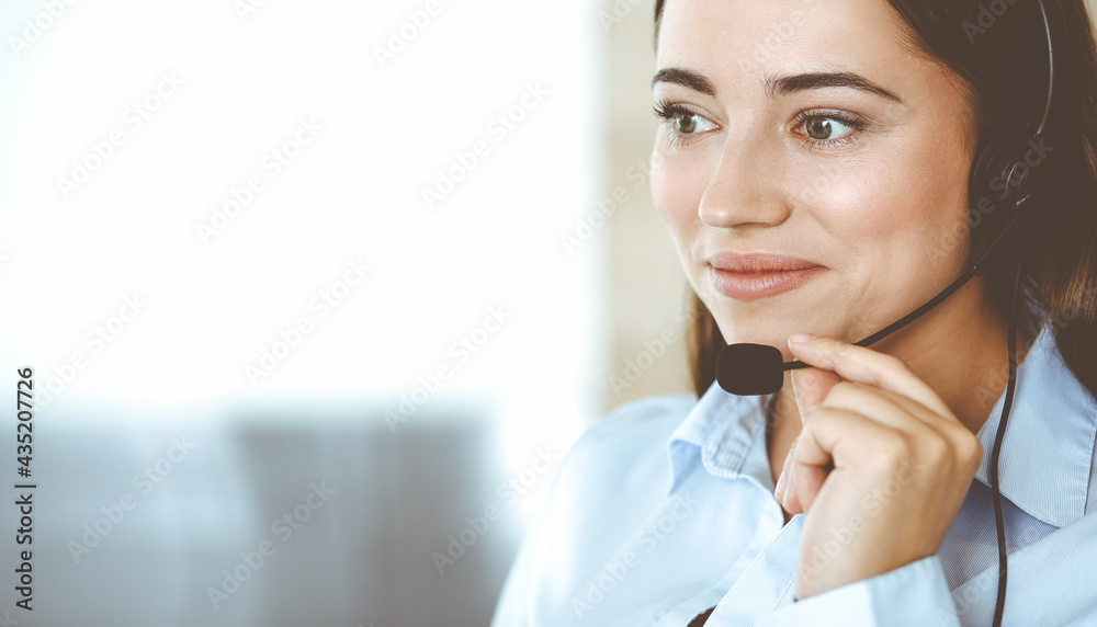 Brunette female customer service representative in a headset is consulting clients online. Call center and business people concept Brunette female customer service representative in a headset is consulting clients online. Call center and business people concept