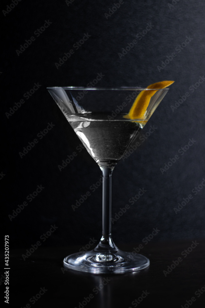 A close up of a martini glass with a drink and an orange peel in it, on a dark background. A close up of a martini glass with a drink and an orange peel in it, on a dark background.