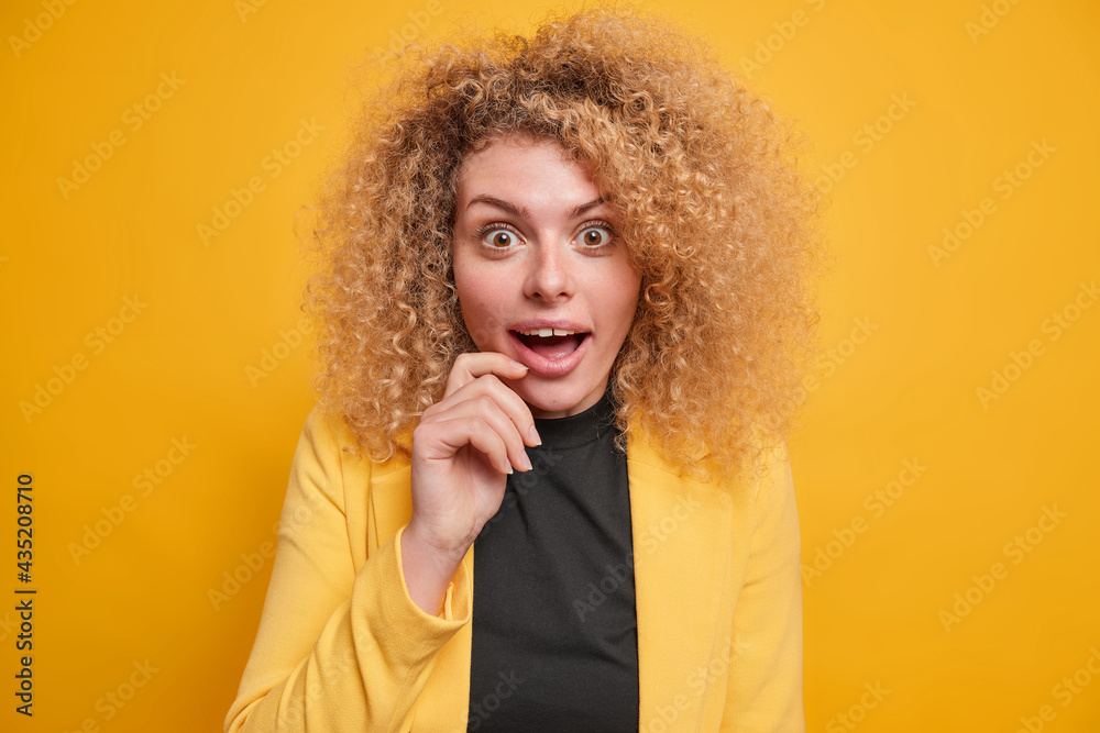 Portrait of surprised curly haired young woman has cheerful happy ...