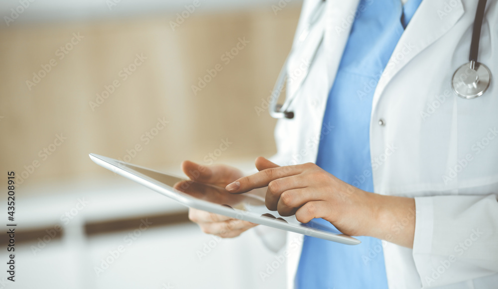 Unknown woman-doctor standing in clinic and using tablet pc, close-up. Data in medicine and healthcare Unknown woman-doctor standing in clinic and using tablet pc, close-up. Data in medicine and healthcare