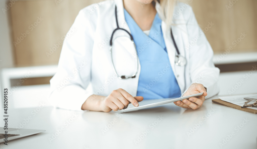Unknown woman-doctor standing in clinic and using tablet pc, close-up. Data and best service in medicine and healthcare Unknown woman-doctor standing in clinic and using tablet pc, close-up. Data and best service in medicine and healthcare