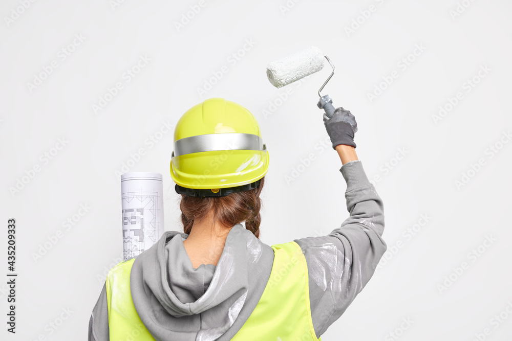 Back view of professional architect busy with design development holds architectural blueprint paints walls with roller wears protective helmet uniform isolated on white background develops new ideas Back view of professional architect busy with design development holds architectural blueprint paints walls with roller wears protective helmet uniform isolated on white background develops new ideas