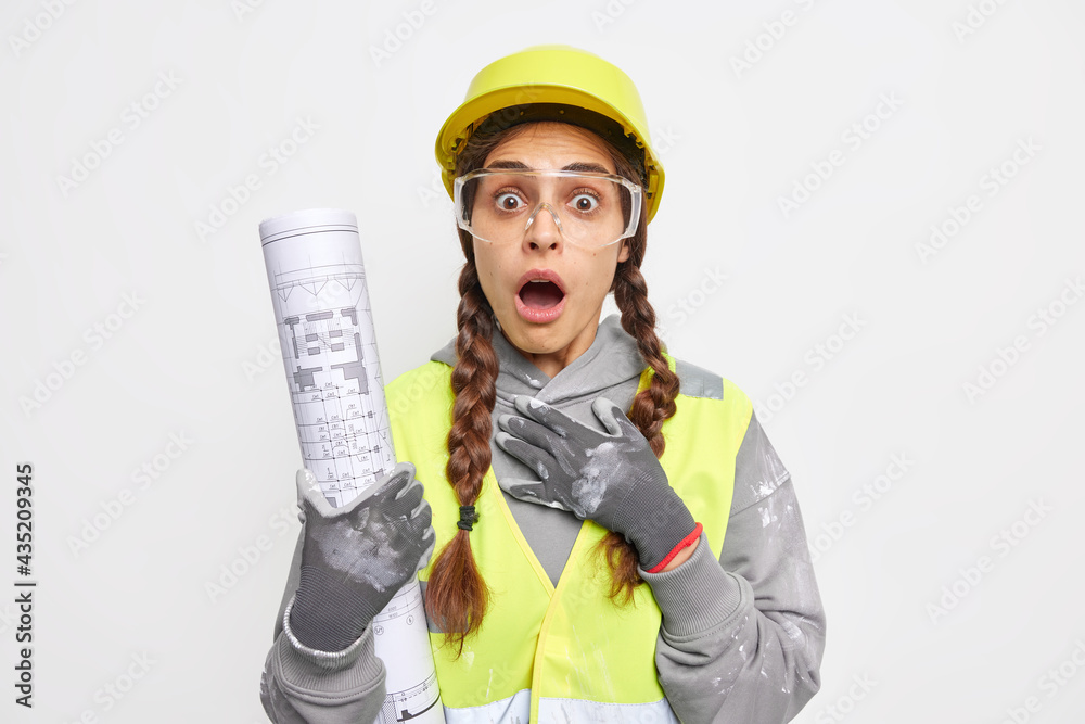Construction industry concept. Shocked female architect builder holds rolled up blueprint has busy working day wears protective uniform stunned to find out some mistake in engineering project Construction industry concept. Shocked female architect builder holds rolled up blueprint has busy working day wears protective uniform stunned to find out some mistake in engineering project