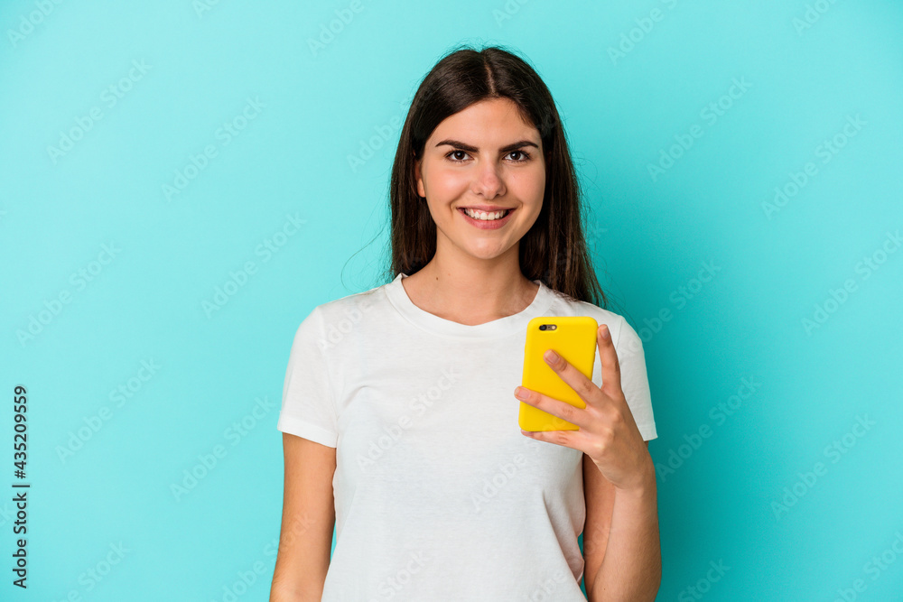 Young caucasian woman holding a mobile phone isolated on blue background happy, smiling and cheerful. Young caucasian woman holding a mobile phone isolated on blue background happy, smiling and cheerful.