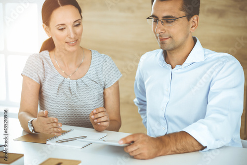 Businessman and hispanic business woman working with computer in sunny office. Group of diverse people