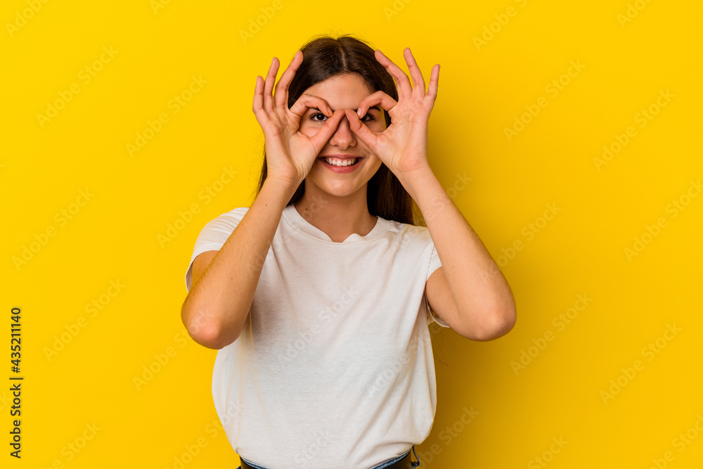 Young caucasian woman isolated on yellow background showing okay sign over eyes Young caucasian woman isolated on yellow background showing okay sign over eyes