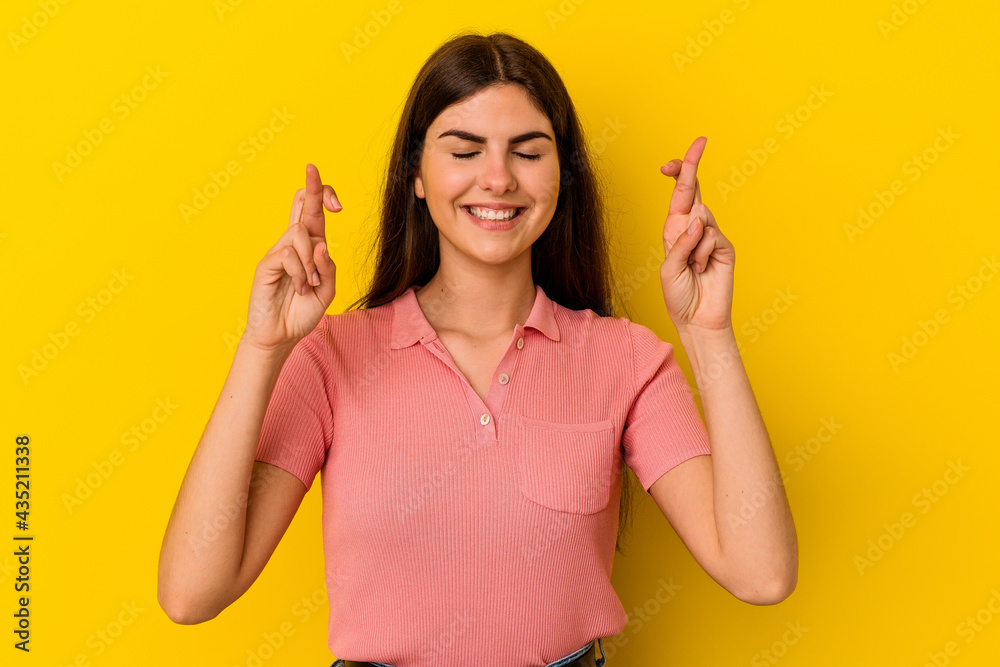 Young caucasian woman isolated on yellow background crossing fingers for having luck