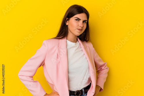 Young caucasian woman isolated on yellow background frowning face in displeasure, keeps arms folded. © Asier