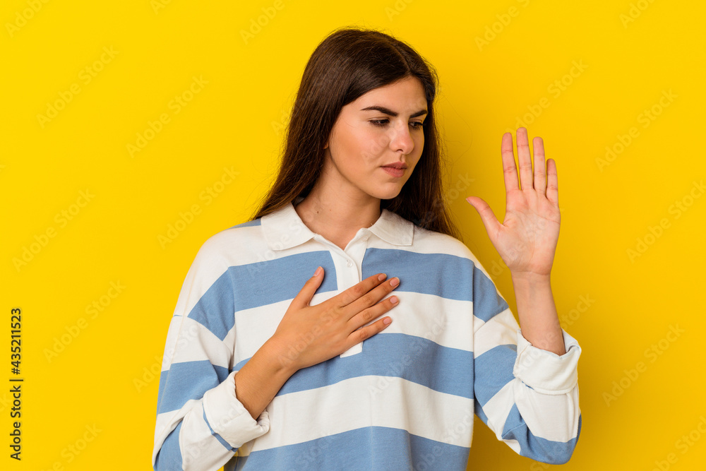Young caucasian woman isolated on yellow background taking an oath, putting hand on chest. Young caucasian woman isolated on yellow background taking an oath, putting hand on chest.