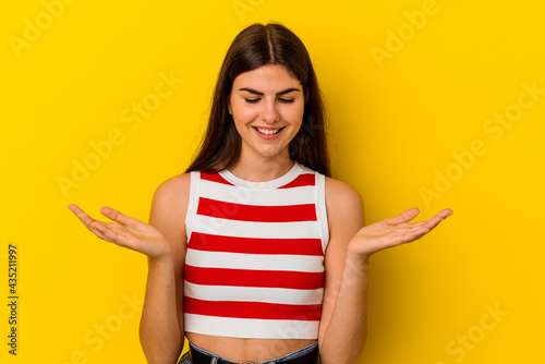 Young caucasian woman isolated on yellow background holding something with palms, offering to camera.