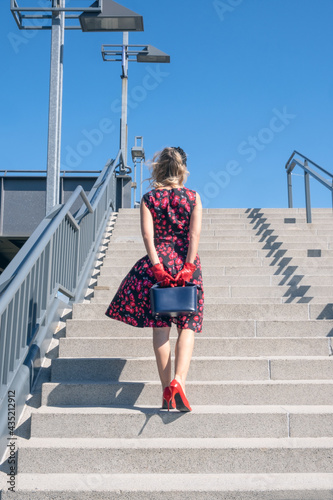 back of blonde woman in red dress walking up stairs outside