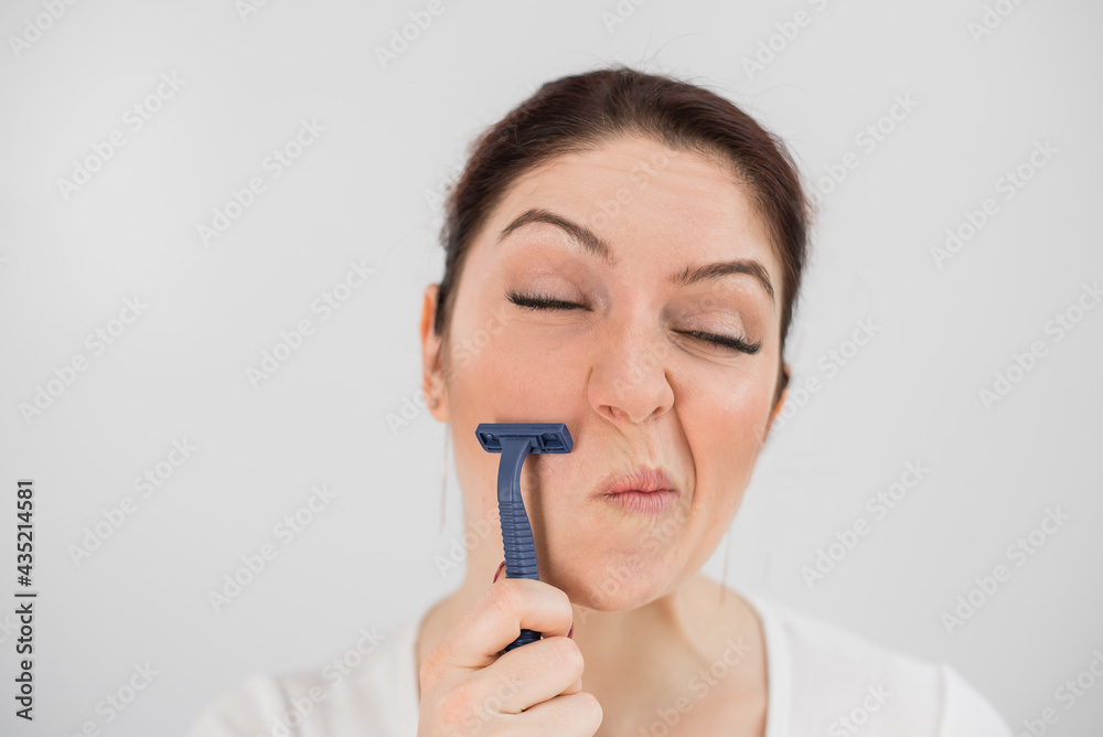 Caucasian funny woman shaves her face with a straight razor on a white background. Copy space. Caucasian funny woman shaves her face with a straight razor on a white background. Copy space.
