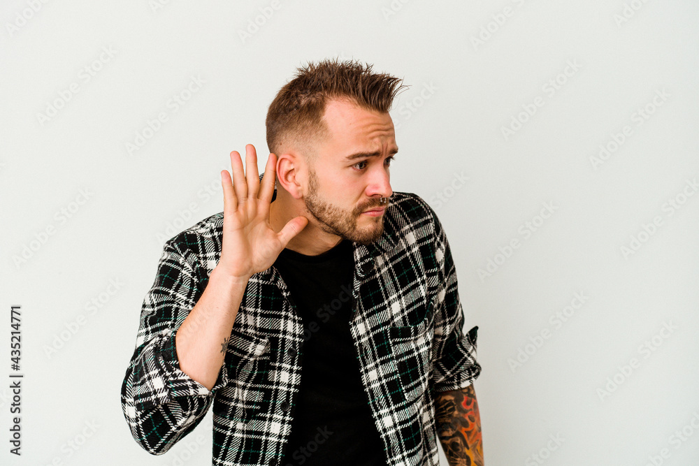 Young tattooed caucasian man isolated on white background trying to listening a gossip. Young tattooed caucasian man isolated on white background trying to listening a gossip.