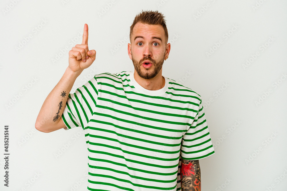 Naklejka premium Young tattooed caucasian man isolated on white background pointing upside with opened mouth.