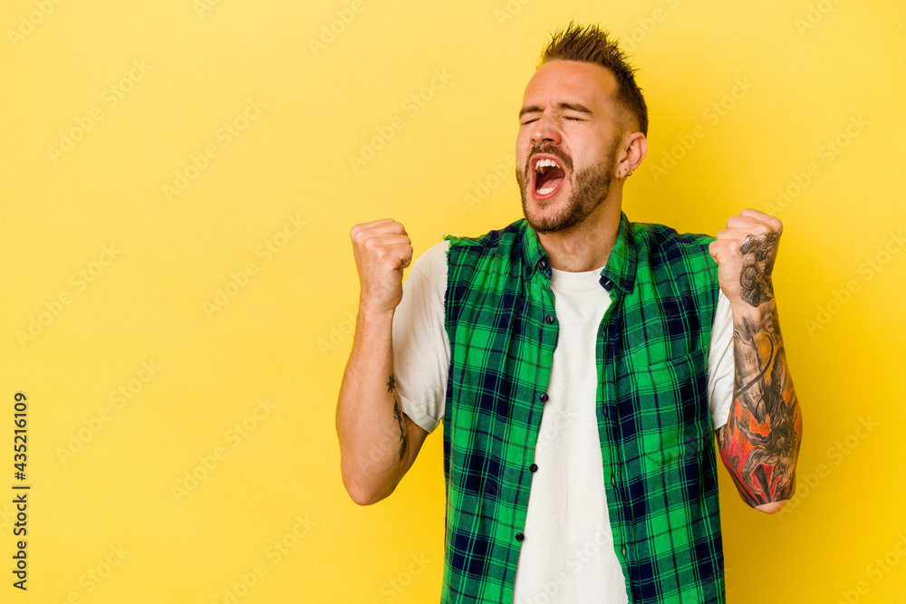 Young tattooed caucasian man isolated on yellow background raising fist after a victory, winner concept. Young tattooed caucasian man isolated on yellow background raising fist after a victory, winner concept.