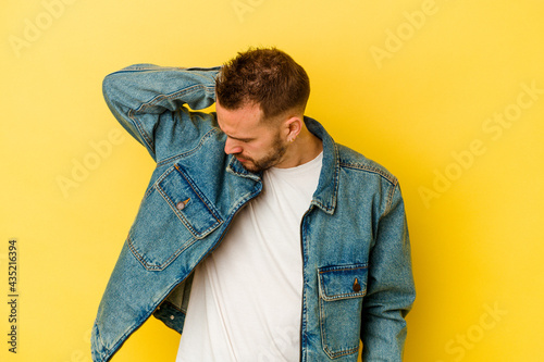 Young tattooed caucasian man isolated on yellow background having a neck pain due to stress, massaging and touching it with hand. © Asier