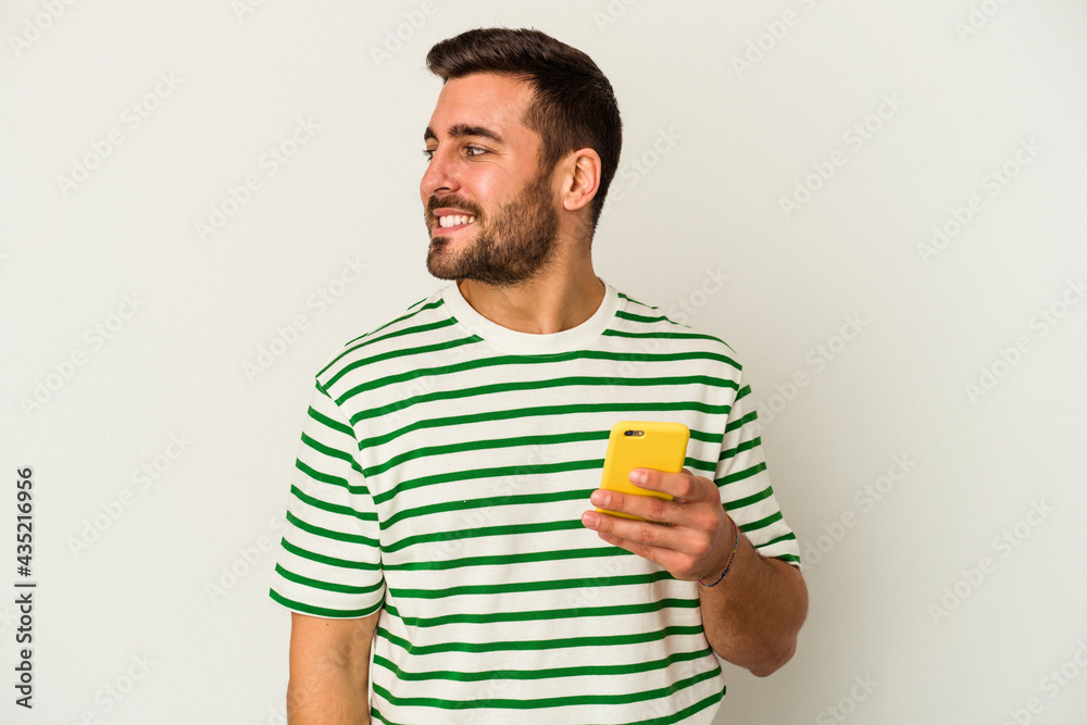 Young caucasian man holding a mobile phone isolated on white background looks aside smiling, cheerful and pleasant. Young caucasian man holding a mobile phone isolated on white background looks aside smiling, cheerful and pleasant.