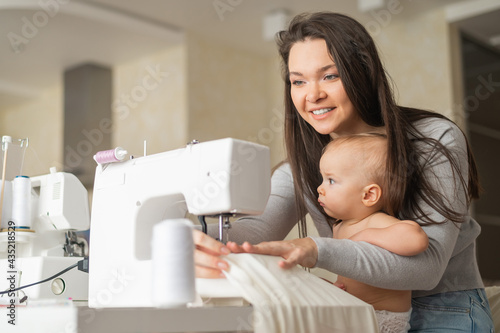 Billede på lærred Young woman sews at home and holds a small child