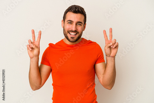 Young caucasian man isolated on white background showing victory sign and smiling broadly.