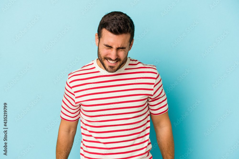 Fototapeta premium Young caucasian man isolated on blue background laughs and closes eyes, feels relaxed and happy.