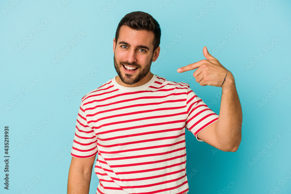 Fototapeta premium Young caucasian man isolated on blue background person pointing by hand to a shirt copy space, proud and confident