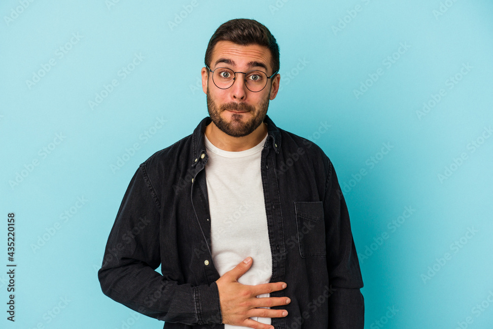 Obraz premium Young caucasian man isolated on blue background touches tummy, smiles gently, eating and satisfaction concept.