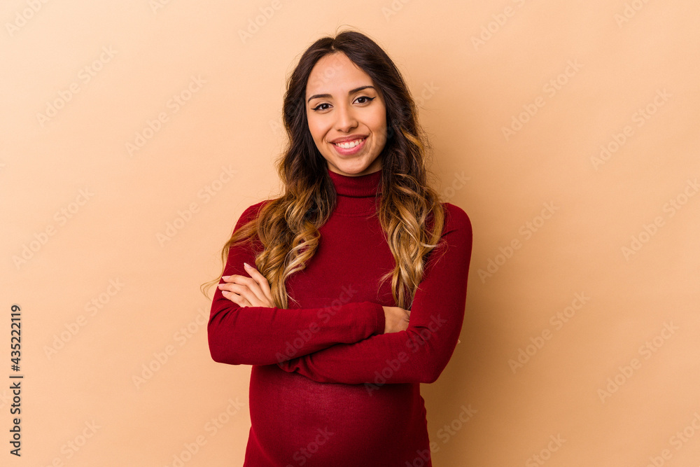 Young mexican pregnant woman isolated on beige background who feels confident, crossing arms with determination. Young mexican pregnant woman isolated on beige background who feels confident, crossing arms with determination.