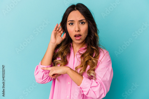 Young mexican woman isolated on blue background trying to listening a gossip.