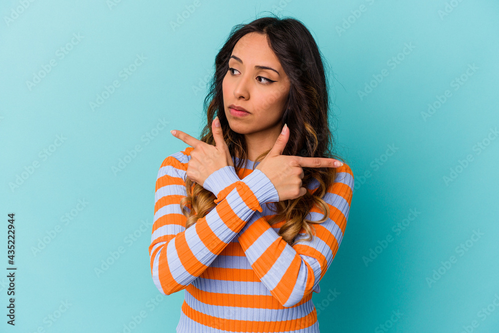 Young mexican woman isolated on blue background points sideways, is trying to choose between two options. Young mexican woman isolated on blue background points sideways, is trying to choose between two options.