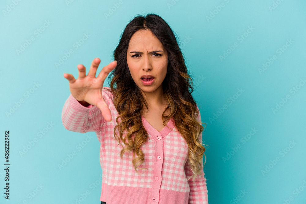 Young mexican woman isolated on blue background showing claws imitating a cat, aggressive gesture. Young mexican woman isolated on blue background showing claws imitating a cat, aggressive gesture.