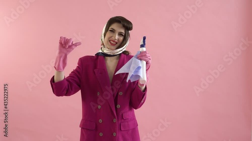 A woman wearing pink rubber gloves holds up a window cleaner spray and gives a thumbs-down gesture. The concept of a home routine. Daily chores around the house. Pin-up style.