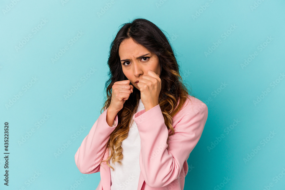 Young mexican woman isolated on blue background throwing a punch, anger, fighting due to an argument, boxing. Young mexican woman isolated on blue background throwing a punch, anger, fighting due to an argument, boxing.