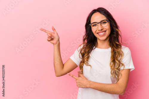 Young mexican woman isolated on pink background pointing with forefingers to a copy space, expressing excitement and desire. © Asier