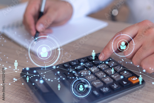 Fototapeta Naklejka Na Ścianę i Meble -  HR specialist researching and analyzing the data of salary on employment market to forecast ongoing expenses of the company using calculator. Hiring new talented officers. Social media hologram icons