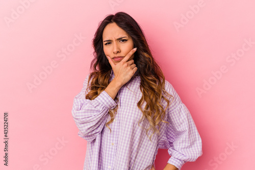 Young mexican woman isolated on pink background contemplating, planning a strategy, thinking about the way of a business. © Asier