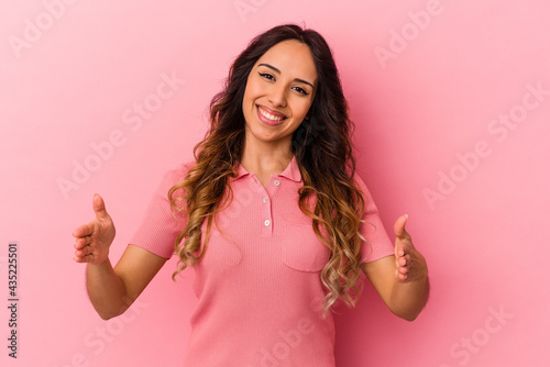 Young mexican woman isolated on pink background holding something with both hands, product presentation. © Asier