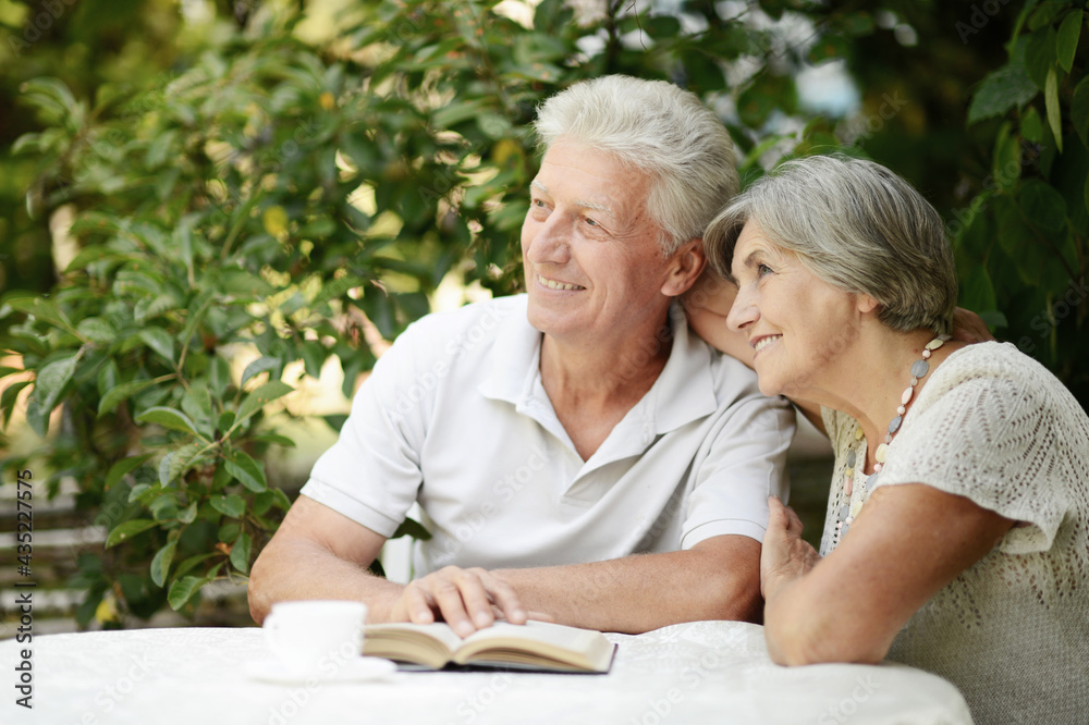 Beautiful old couple reading book at table in summer Beautiful old couple reading book at table in summer