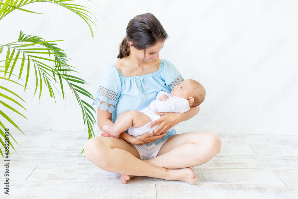 a young mother with a newborn baby gently holds it in her arms, hugging and admiring it at home, the concept of a happy family and the birth of children