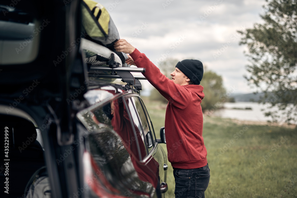 Windsurfer and camper packing and unpacking from a car's roof rack in nature.