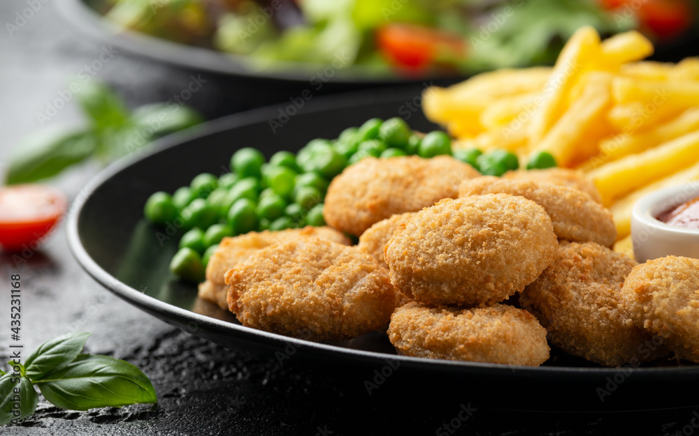 Fried crispy chicken nuggets with ketchup, french fries and green peas in black plate Fried crispy chicken nuggets with ketchup, french fries and green peas in black plate