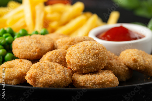 Fried crispy chicken nuggets with ketchup, french fries and green peas in black plate