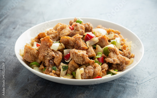 Stir fry chinese salt and pepper chicken with red, green chilli, onion, spring onion in white bowl.