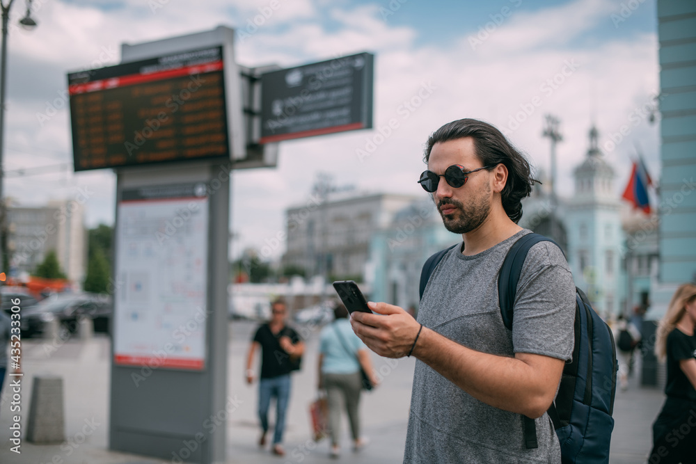 A man looks at the phone at the train schedule at the station A man looks at the phone at the train schedule at the station