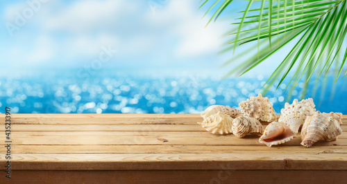 Fototapeta Naklejka Na Ścianę i Meble -  Summer background with wooden table, seashells and palm tree over sea beach bokeh. Tropical vacation concept