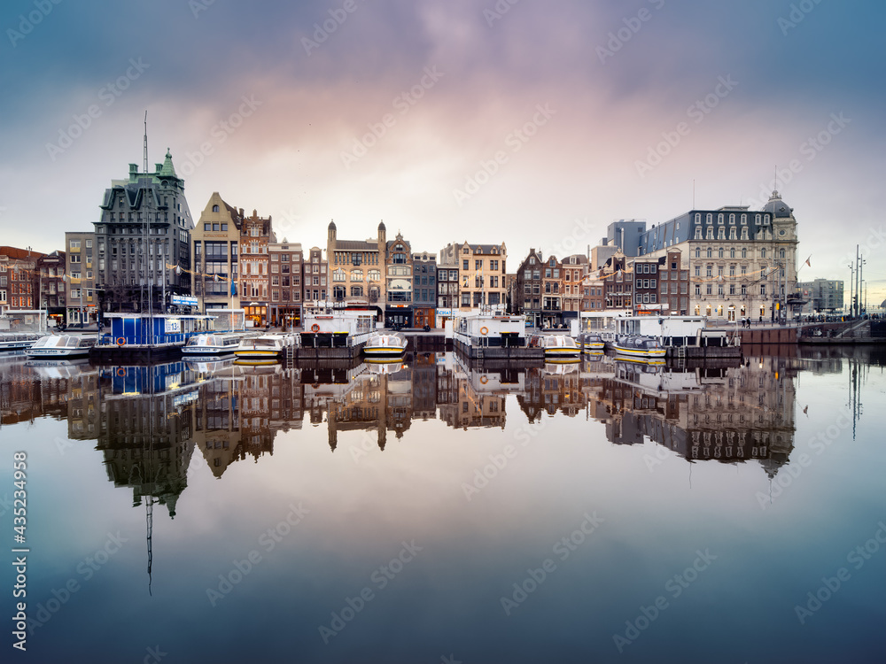 Reflection of historic canal houses and tourist canal boats in the Damrak canal in Amsterdam.