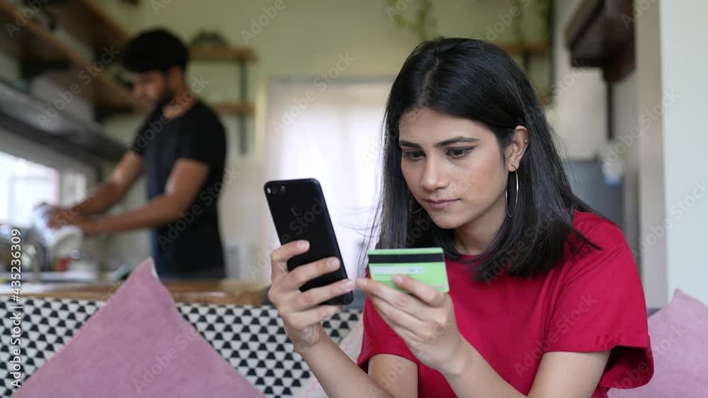 Asian lady using phone,credit card buy and purchase e-commerce internet at home while man work hard in kitchen.Stay at home,online shopping,social distancing,quarantine for corona virus prevention. Asian lady using phone,credit card buy and purchase e-commerce internet at home while man work hard in kitchen.Stay at home,online shopping,social distancing,quarantine for corona virus prevention.