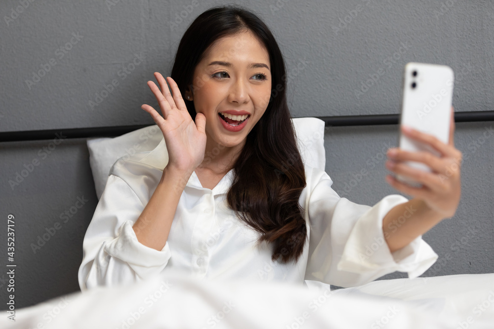 young beautiful woman sitting on bed, taking photo, selfie or talking online to someone from smartphone young beautiful woman sitting on bed, taking photo, selfie or talking online to someone from smartphone